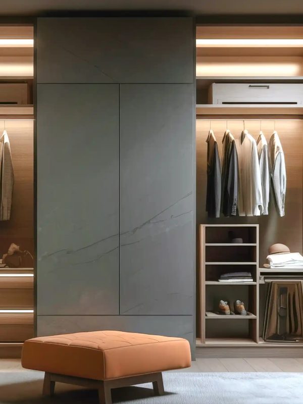 A spacious walk-in closet featuring warm wood cabinetry, hanging clothes, and an orange bench.